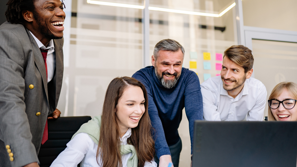 Diverse recruitment team collaborating around a computer screen reviewing career site candidate data in a modern office